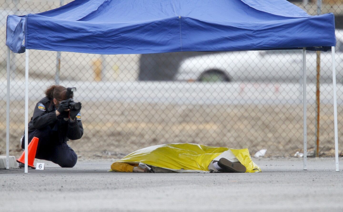 A crime scene investigator photographs a body in the parking lot of the Micro Center computer store in Tustin.