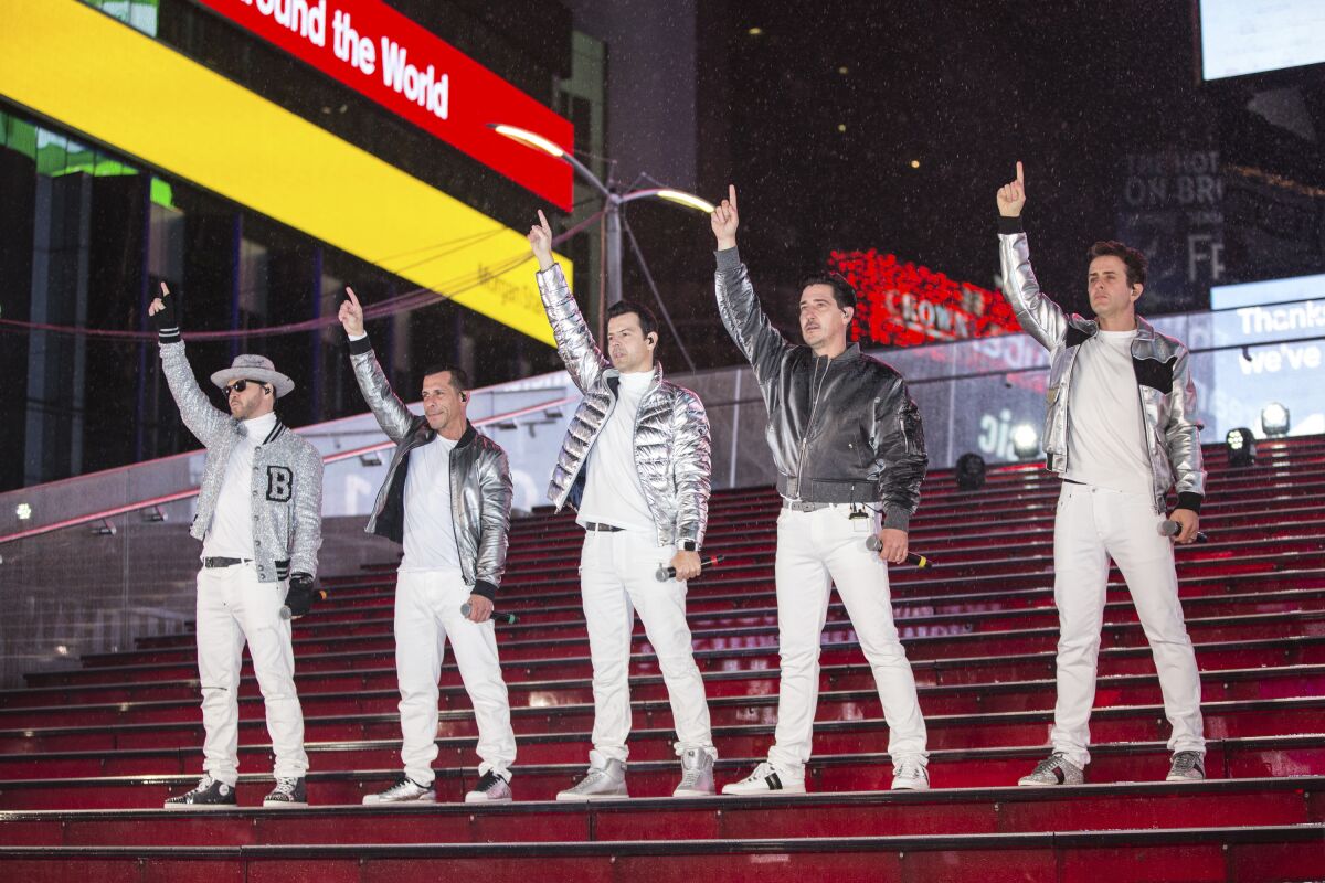 Five men in white-and-silver outfits stand on a red staircase and point to the sky