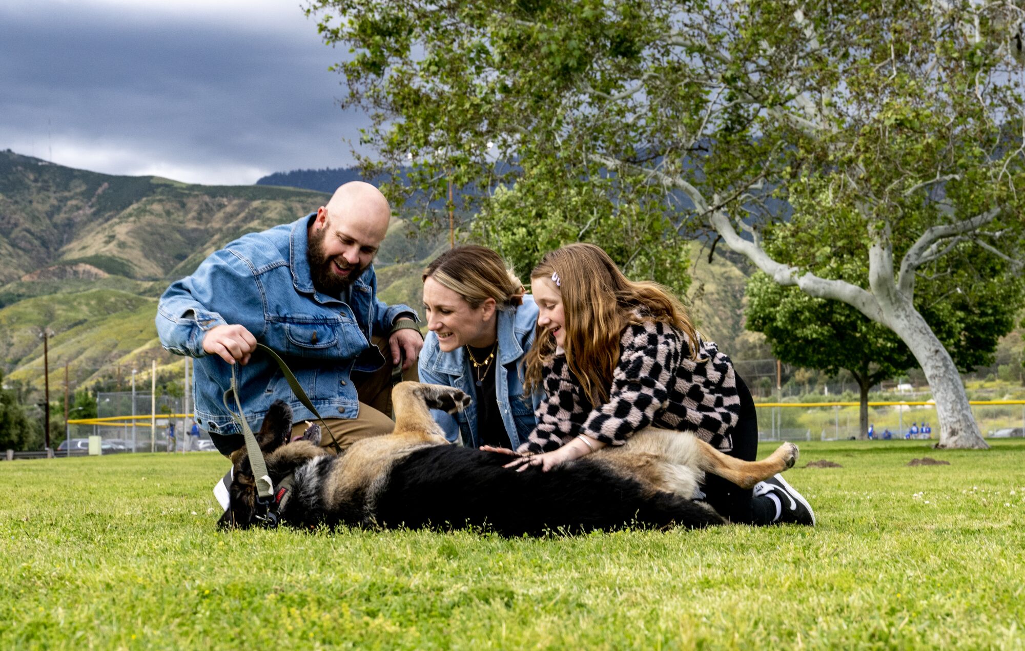Three Bauer family members rub a German shepherd's belly at the park.