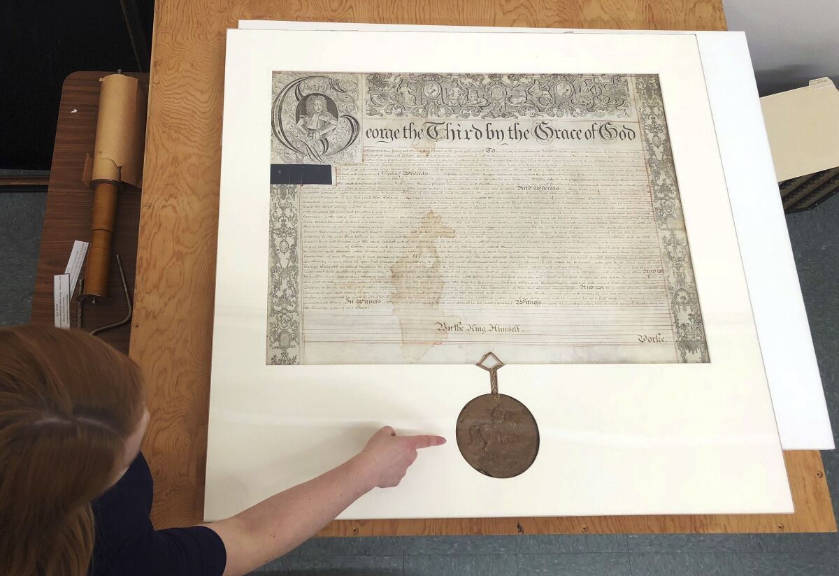 FILE - Rhode Island state archivist Ashley Selima points to the seal of King George III on a September 1772 proclamation in Providence, R.I., May 24, 2018. The document established a commission to investigate the burning of the British schooner HMS Gaspee by colonists in Narraganset Bay in June 1772. A new effort is underway to find the remains of the British ship that Rhode Island colonists burned 250 years earlier, marine archeologists and state officials announced, Tuesday, May 10, 2022. (AP Photo/Jennifer McDermott, File)