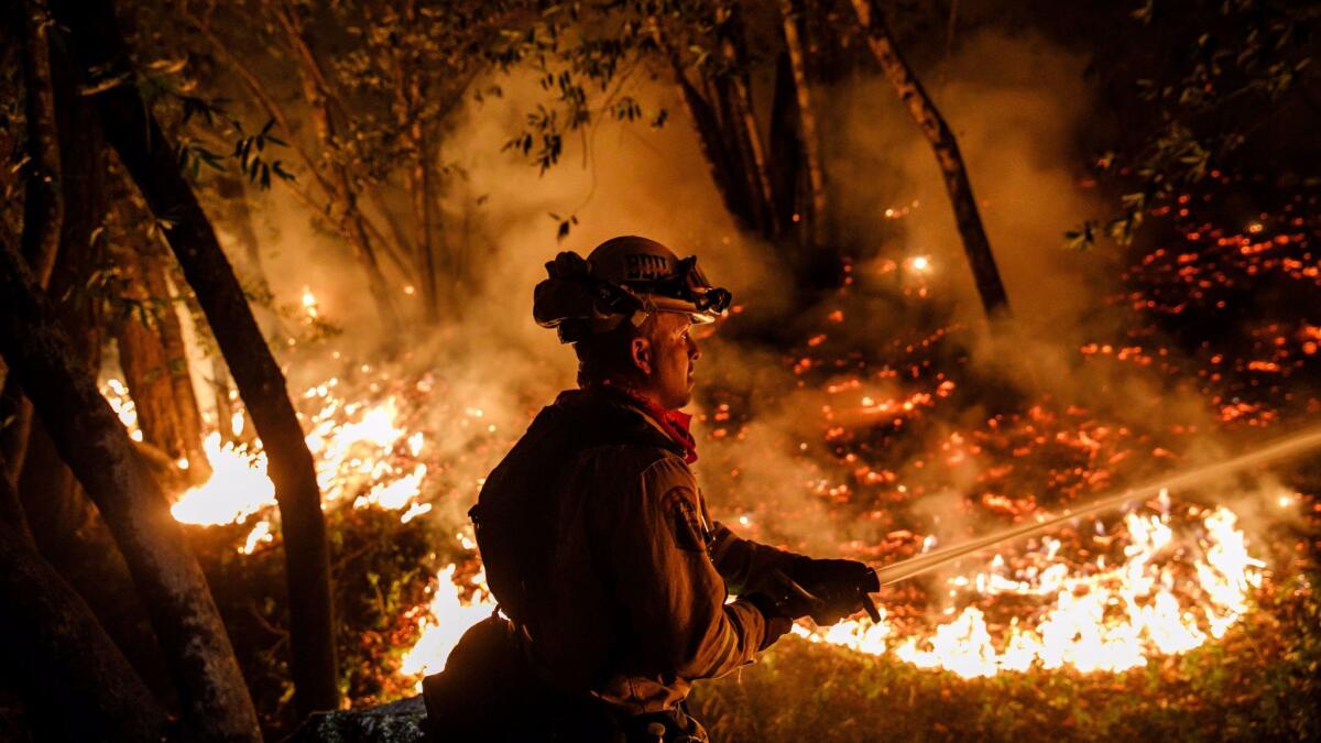 Cal Fire firefighter Mario Topete sprays water to help prevent flames from crossing Highway 29, north of Calistoga, on Thursday.