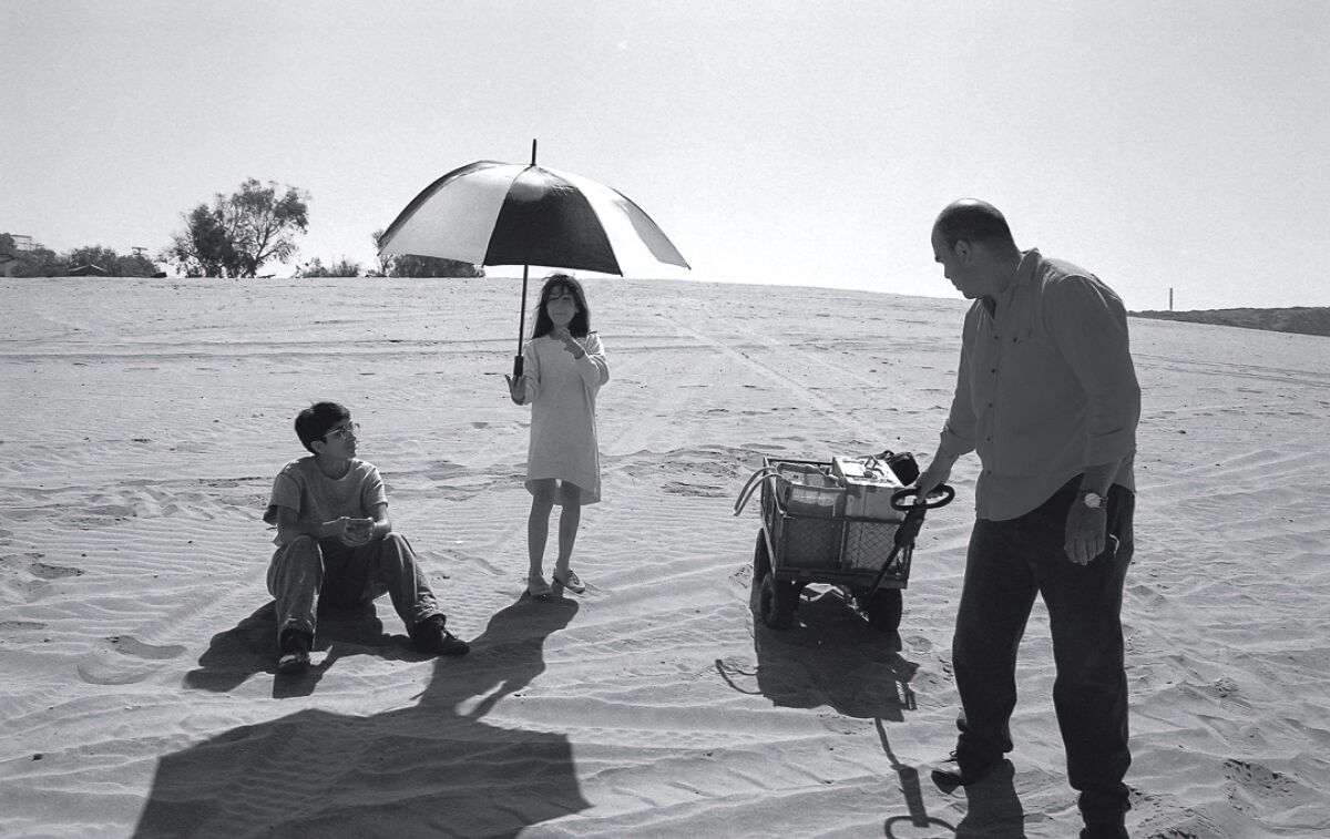 A man shooting a film on a beach with girl holding an umbrella