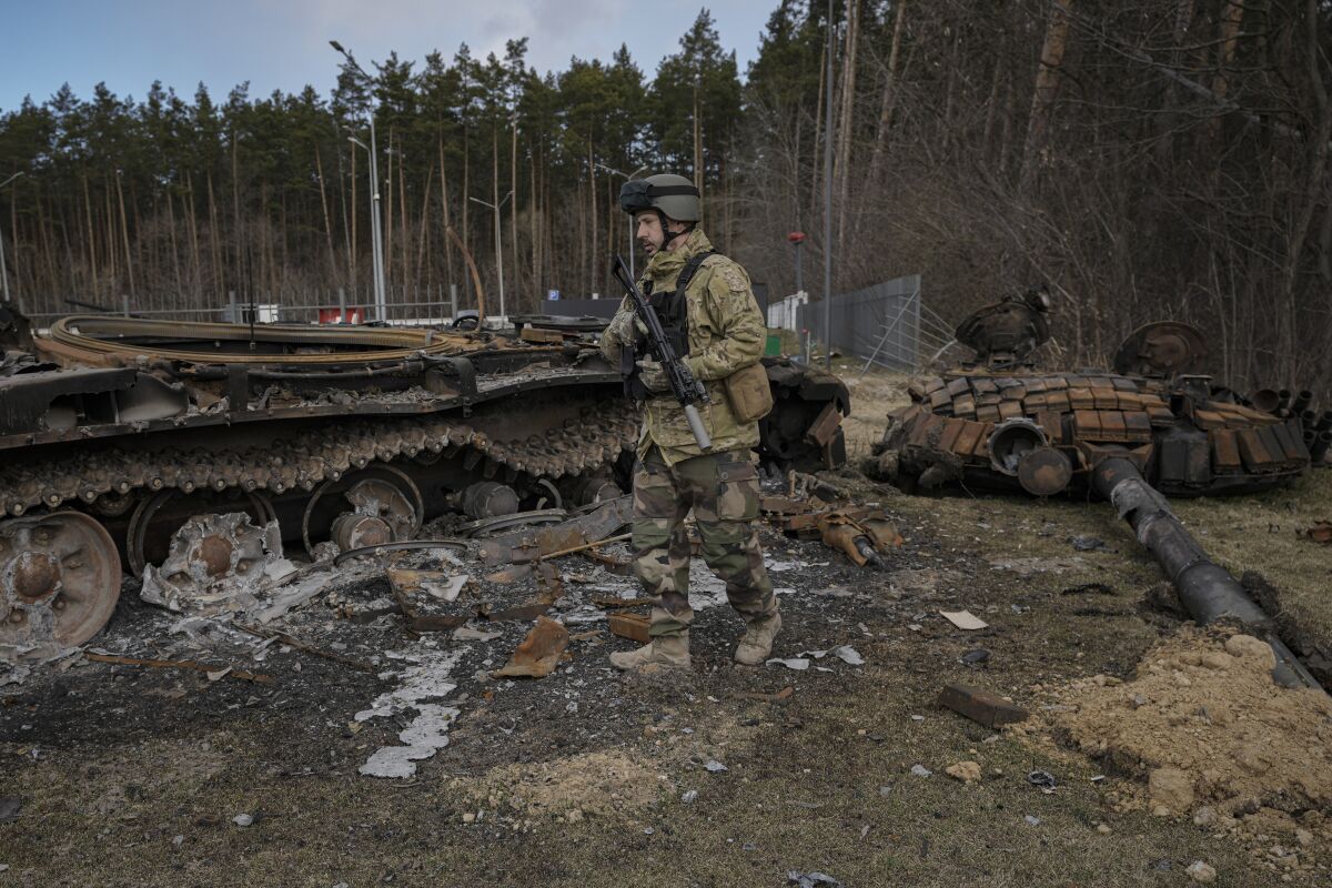 An armed man in fatigues walks next to a destroyed tank