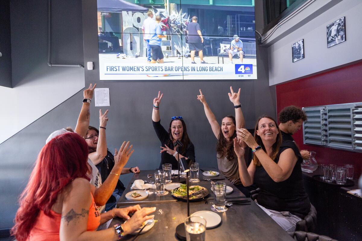 Patrons cheer a televised news report during the grand opening of Watch Me! Sports Bar in Long Beach