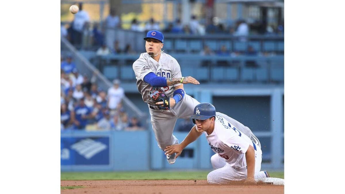 Cubs Javier Baez is forced into a throwing error while trying to complete a double play as Corey Seager slides into him.