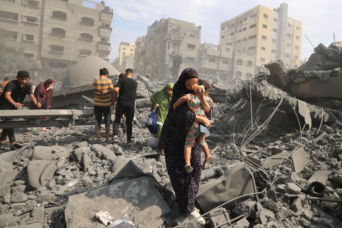 A woman carries a child through rubble in Gaza City