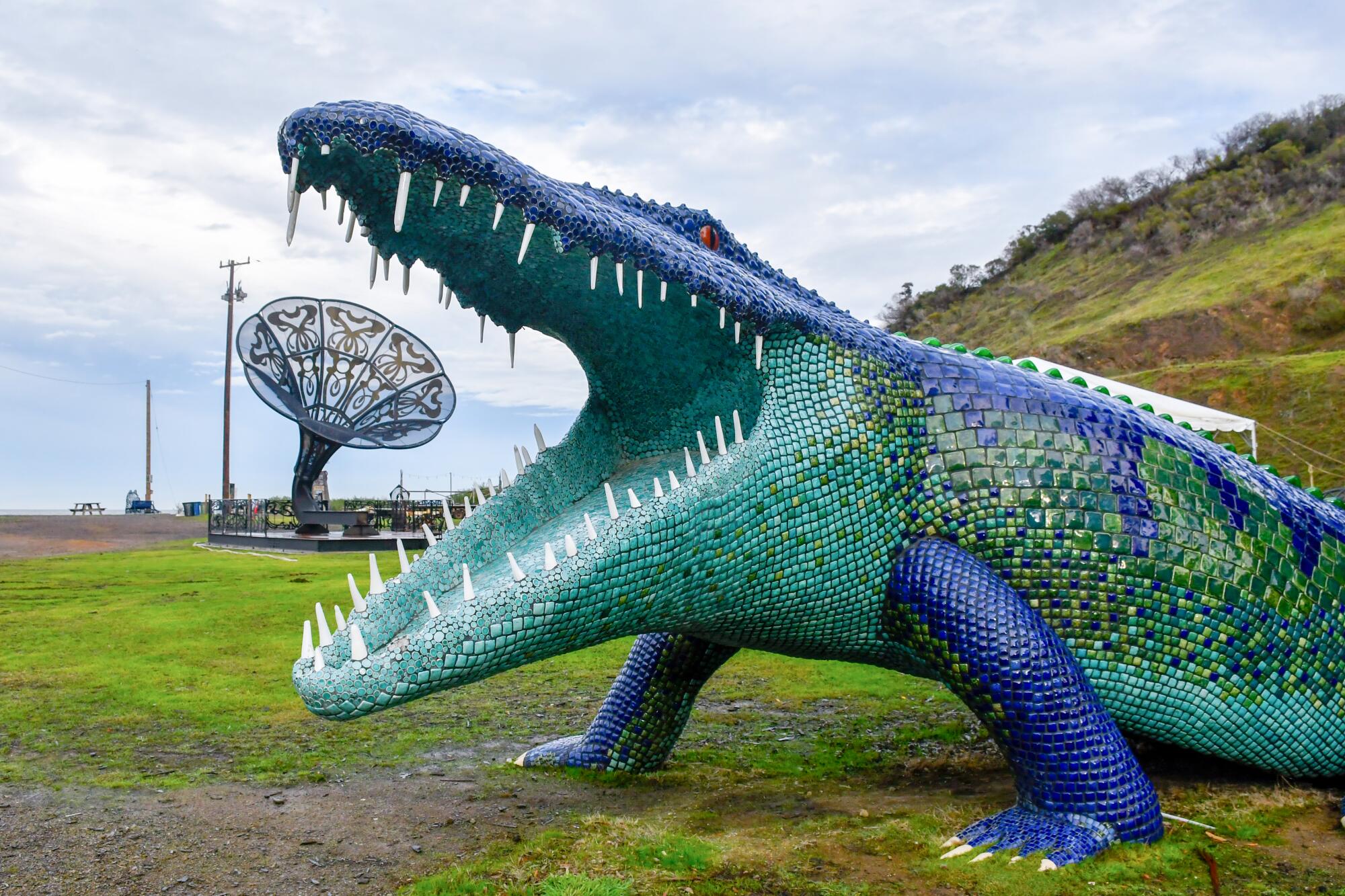 A blue and green mosaic-decorated crocodile statue, jaws open wide.