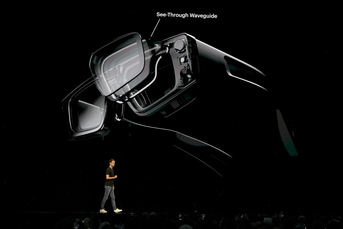 a man speaks onstage in front of a large image of smart glasses