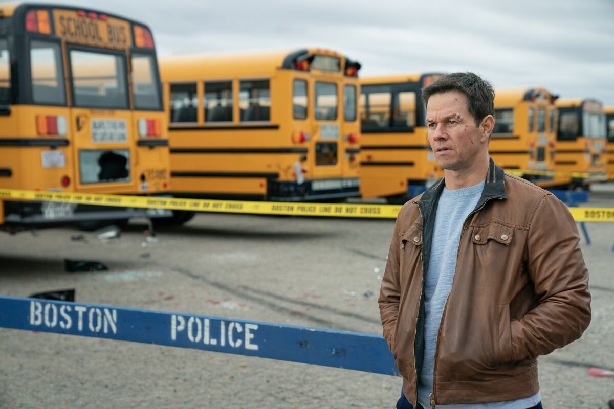 Mark Wahlberg in "Spenser Confidential" stands by a Boston Police barricade, caution tape, school buses.