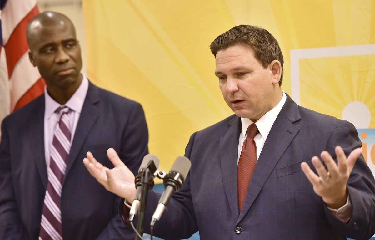 Florida Gov. Ron DeSantis addresses the media as Dr. Joseph Ladapo, Florida surgeon general, looks on during a news conference in Jacksonville, Fla., on Tuesday, Jan. 4, 2022 to discuss COVID-19 testing policy and monoclonal antibody treatment availability. The event was relocated from the Department of Children and Families office building to the adjacent FDLE building after protesters, wanting to address the governor, refused to leave the initial news conference site. (Bob Self/The Florida Times-Union via AP)