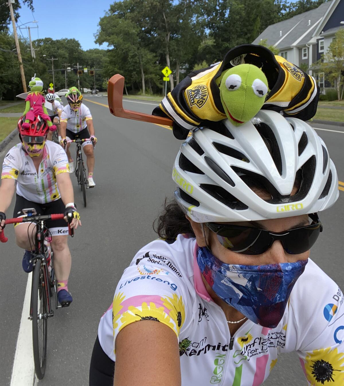 In this July 31, 2020 photo, Pan-Mass Challenge bike rider Celia Donatio, right, cycles with her teammates through Needham, Mass. "Team Kermit" raised close to $554,000 for Dana Farber Cancer Research. PMC founder Billy Starr knew he wouldn't be able to get 10,000 people together this summer for the annual cross-state bike ride that has raised more than $700 million for cancer research. But he also knew he couldn't take the year off. While other events in the $1.4 billion participatory fundraising field shut down during the coronavirus outbreak, the PMC delivered $50 million for the Dana-Farber Cancer Institute. (Photo by Celia Donatio via AP)