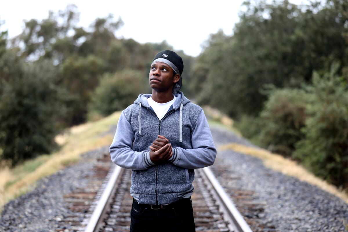 A man looks up with his hands clasped while standing on railroad tracks
