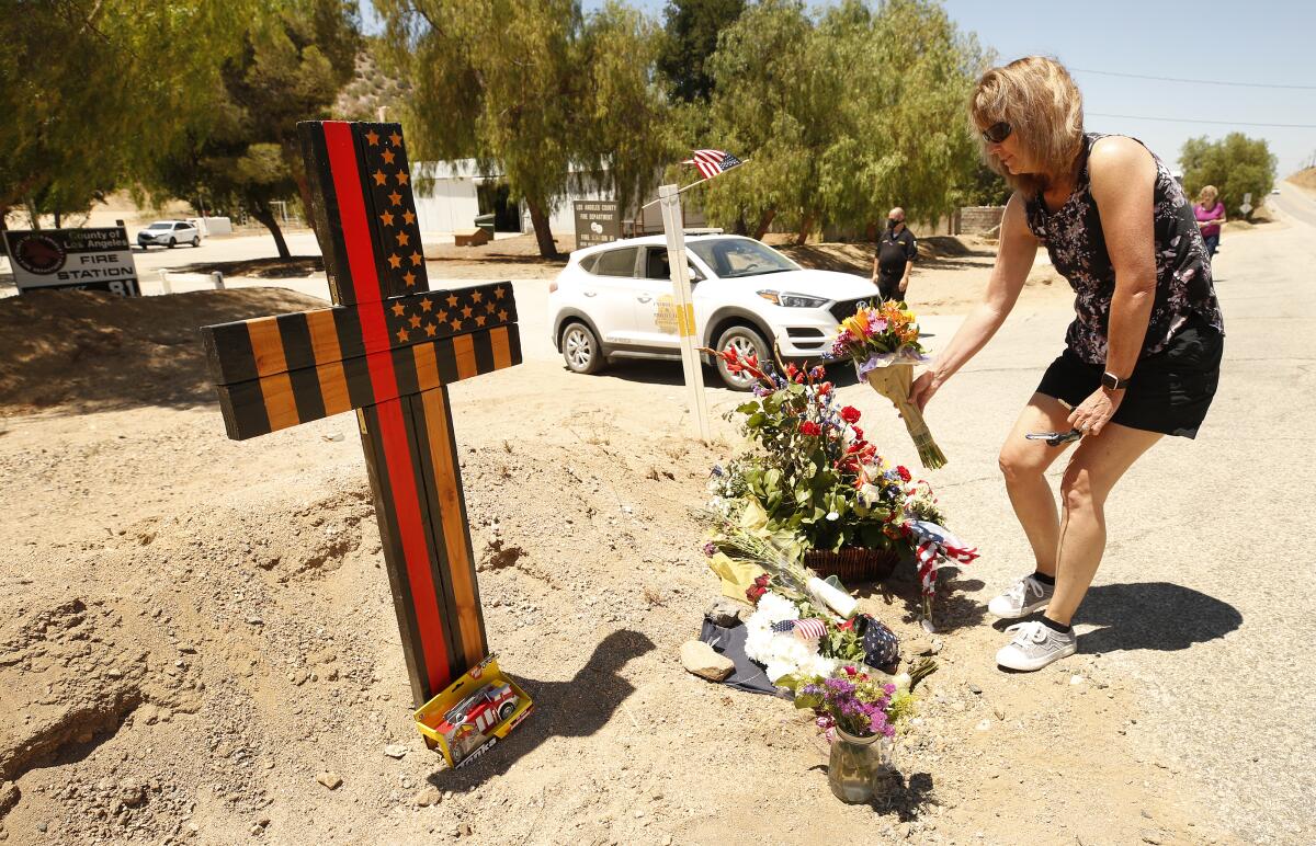 A woman places flowers in front of a wooden cross in the dirt