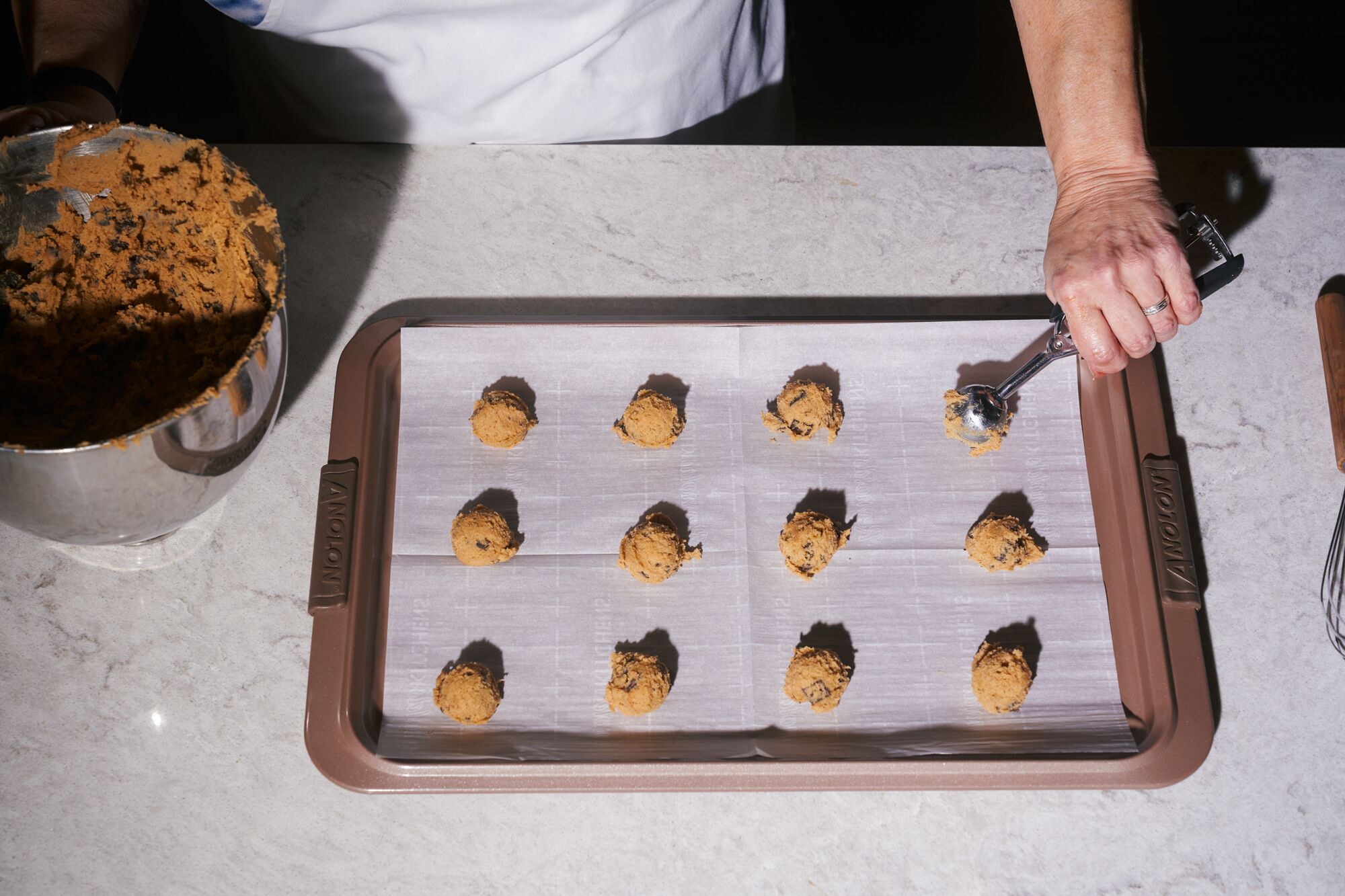 A hand scoops cookie dough onto a parchment paper-lined baking sheet.