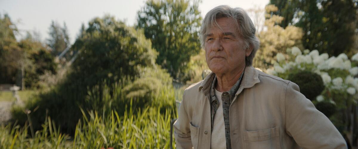 Lee Show stands in a khaki jacket and white T-shirt in a field surrounded by trees.