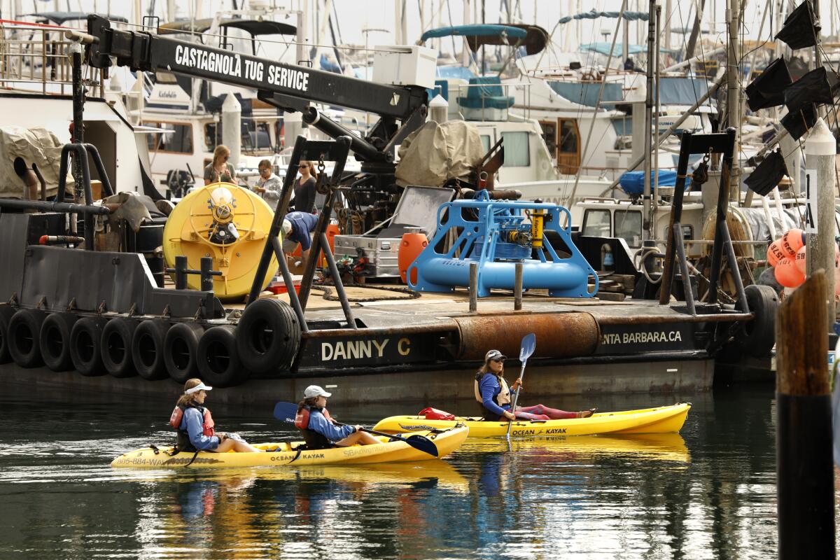 Kayakers in the Santa Barbara Harbor pass by a tug boat that holds a new whale monitoring system before it is deployed in the channel.