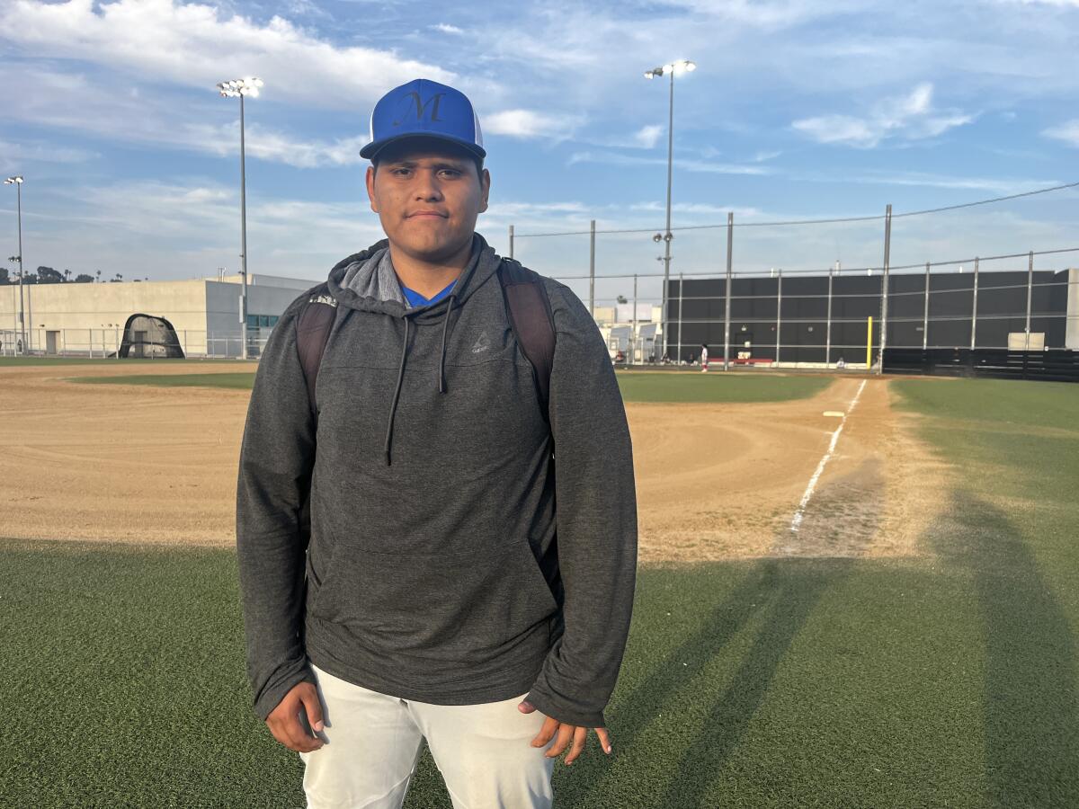 Maywood Academy pitcher Samuel Loza stands in front of a baseball field.
