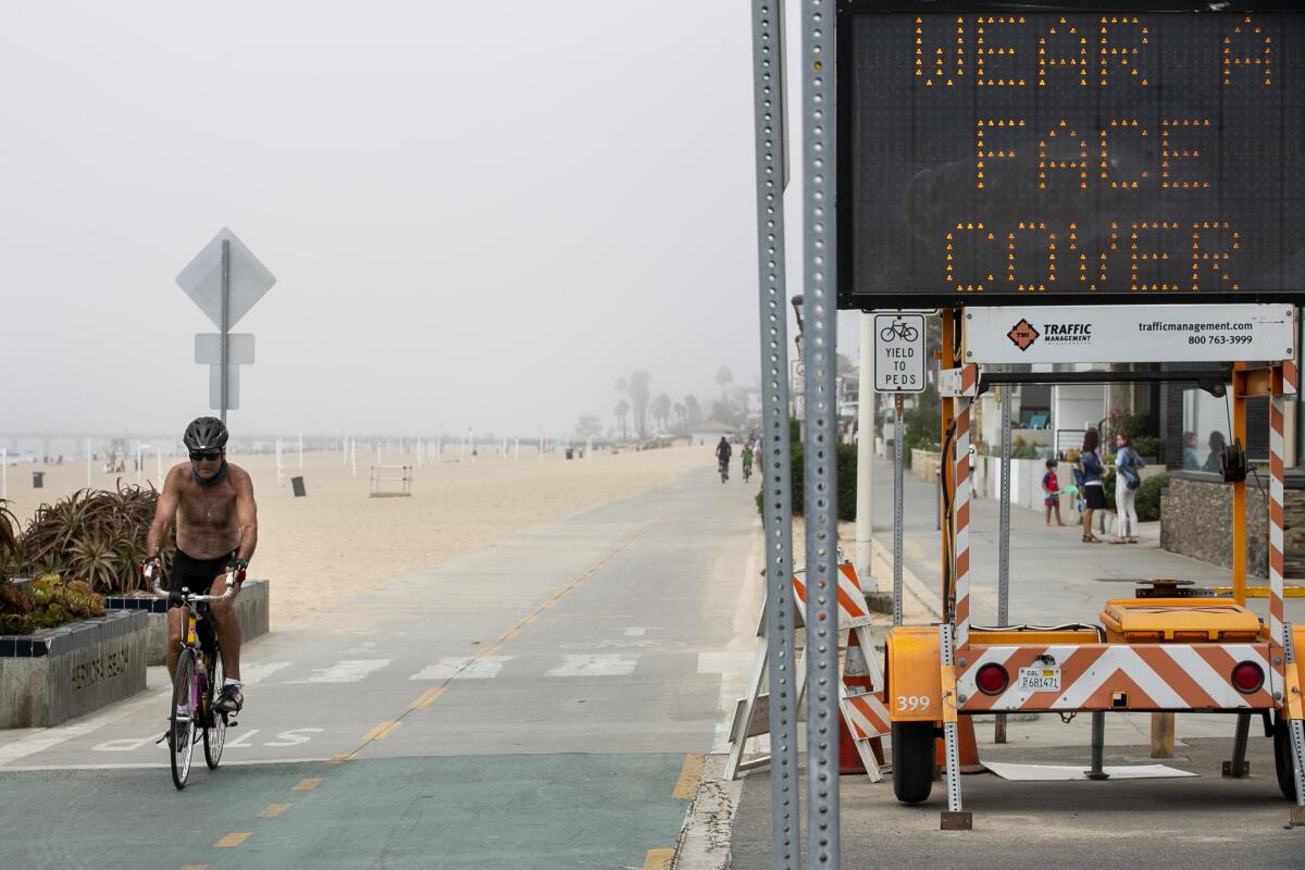 A cyclist passes a sign advising beachgoers to wear masks in Hermosa Beach in September.