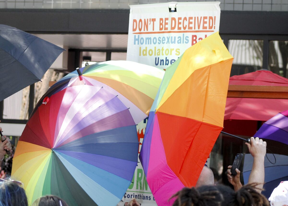 FILE - A sign-carrying anti-gay protester is surrounded by a sea of Pride umbrellas during the Pride parade in Winston-Salem, N.C., June 18, 2022. Hateful references to gays, lesbians and other LGBTQ Americans on social media surged following Florida's adoption of a law restricting how teachers can talk about sexual orientation with younger students. (AP Photo/Skip Foreman, File)