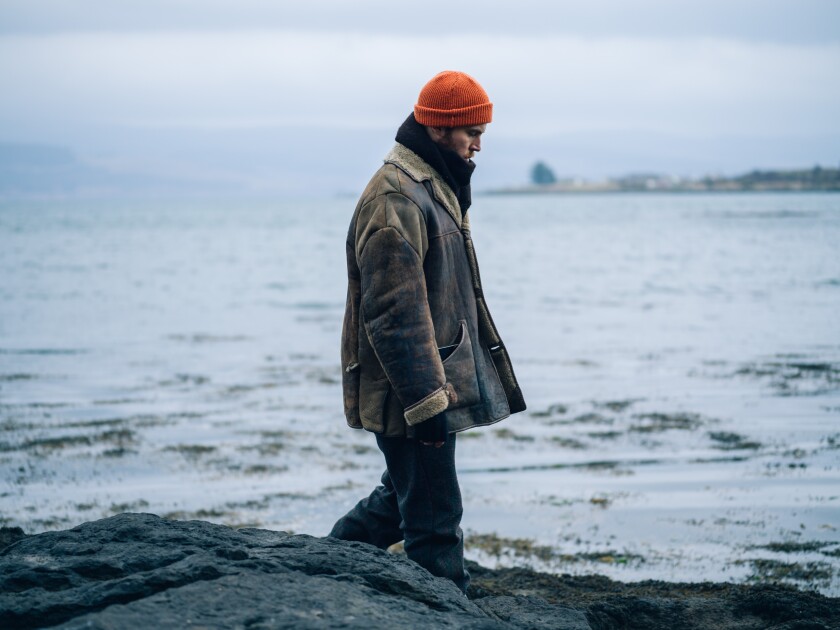 A man in a cap and coat walks along a shoreline in the movie "Shepherd."