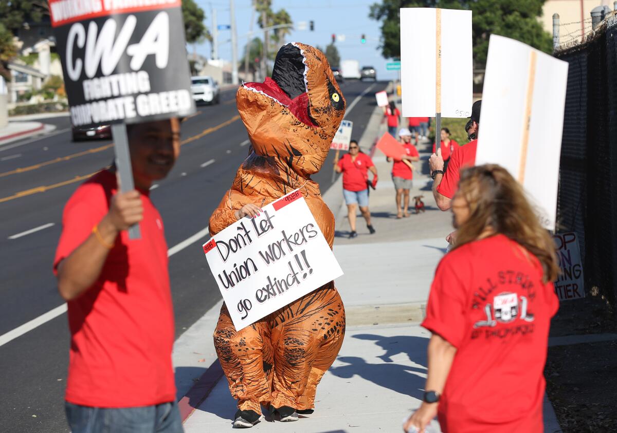 A Communications Workers of America employee wears a dinosaur costume outside the Huntington Beach Frontier office Thursday.