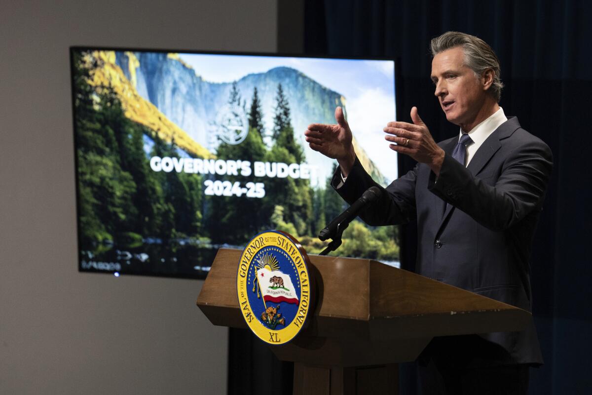 California Gov. Gavin Newsom at a lectern near a monitor that shows a slide labeled Governor's Budget