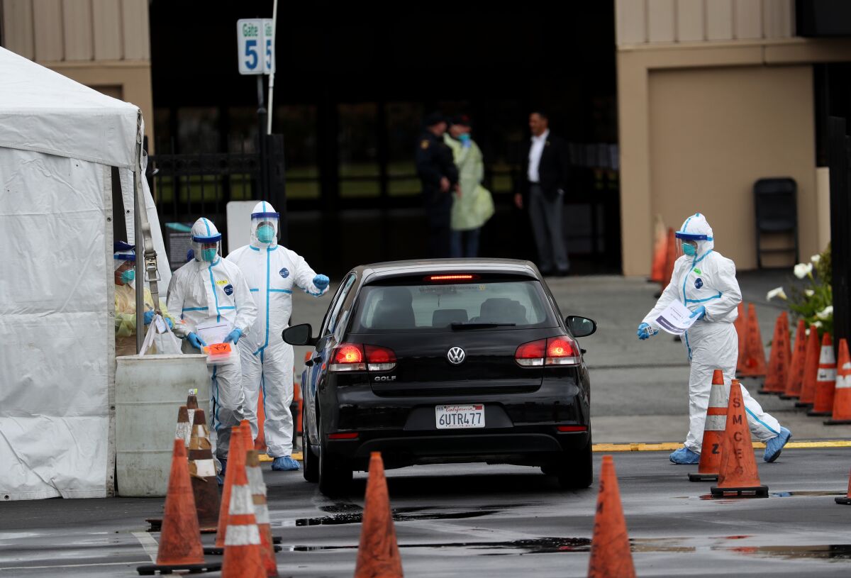 Medical workers in full-body protective gear around a car at a drive-through testing site
