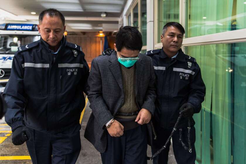 Deyun Shi is escorted by police to a hospital in Hong Kong prior to being returned to L.A.