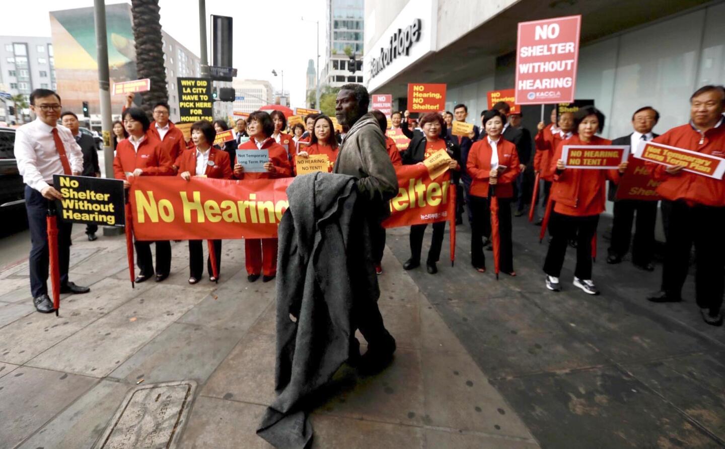 A homeless man stands in front of protesters who are marching against a planned temporary homeless shelter in Koreatown at Wilshire Boulevard and Vermont Avenue.