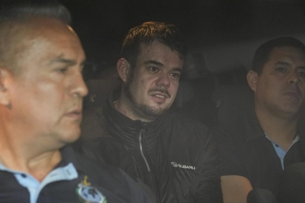 A man sitting in a vehicle between two law enforcement officers.