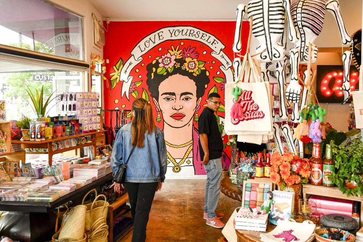 People browse in a shop before a wall painted with Frida Kahlo's face and the words "Love Yourself."