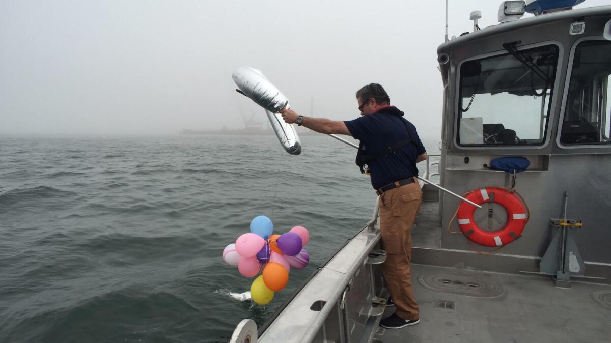 John Giles, Marina del Rey district manager for the L.A. County Department of Beaches and Harbors, fishes helium-filled balloons out of the water near the marina channel breakwater.