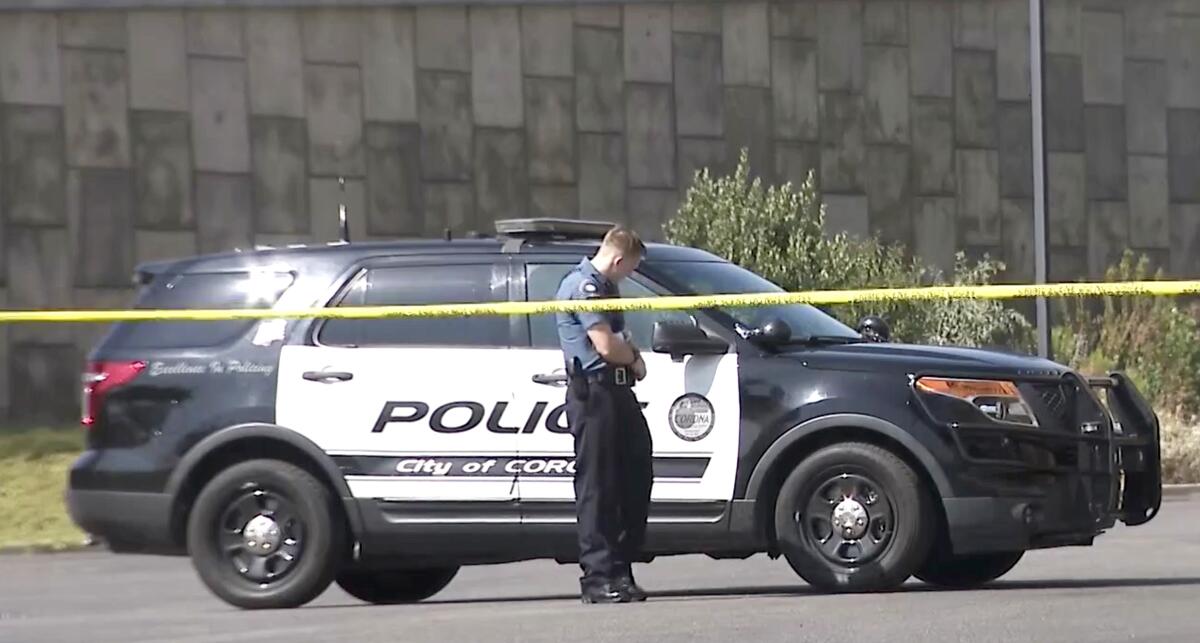 Policeman stands behind yellow crime scene tape and in front of a police vehicle.