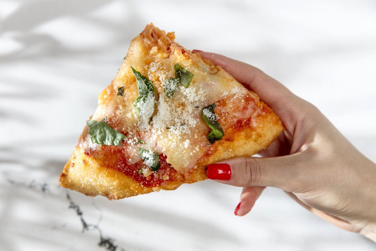 A slice of pizza is held in a woman's hand