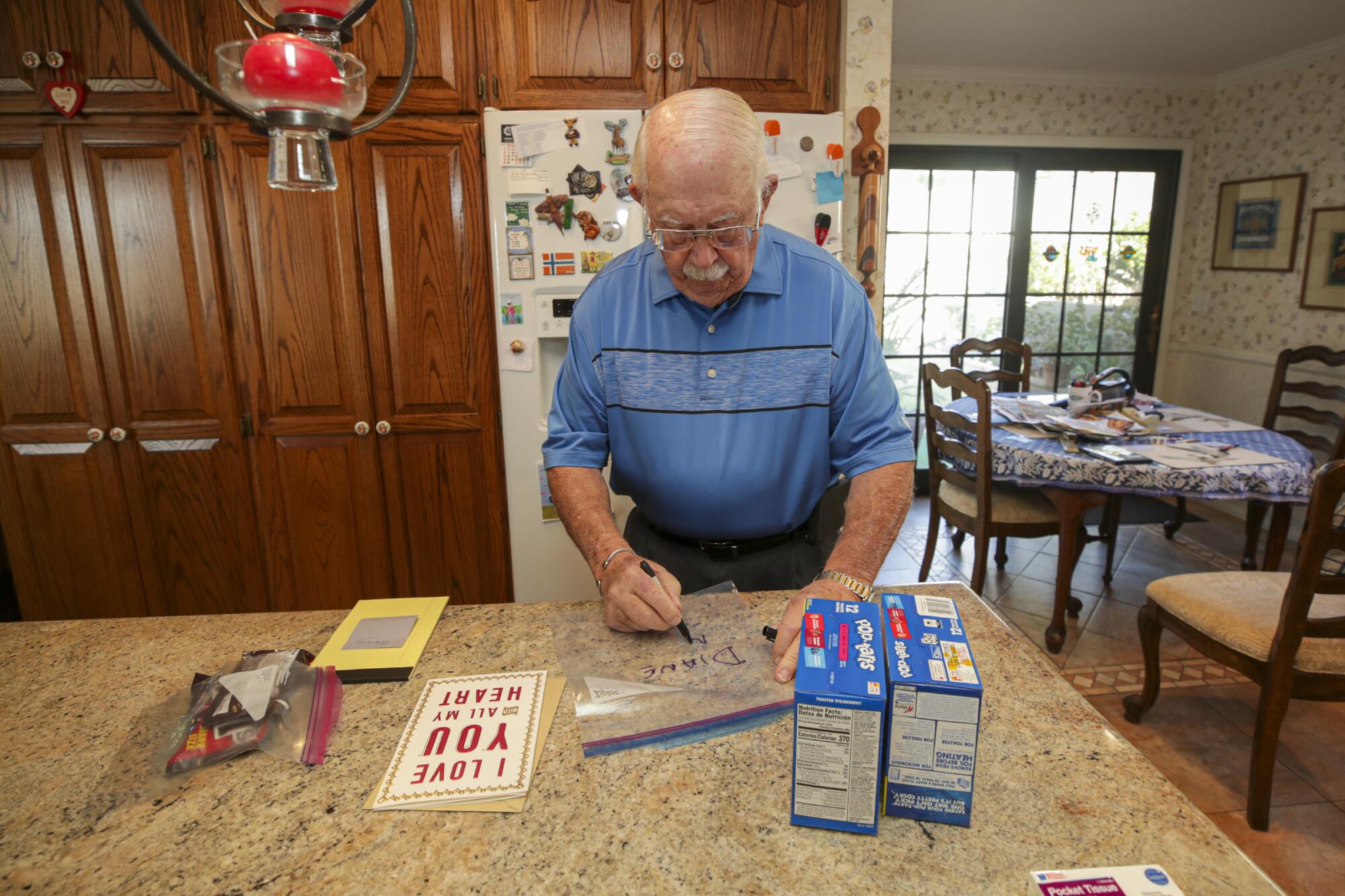 A man writes the name Diane on a Ziploc bag next to a Valentine's card and boxes of Pop-Tarts