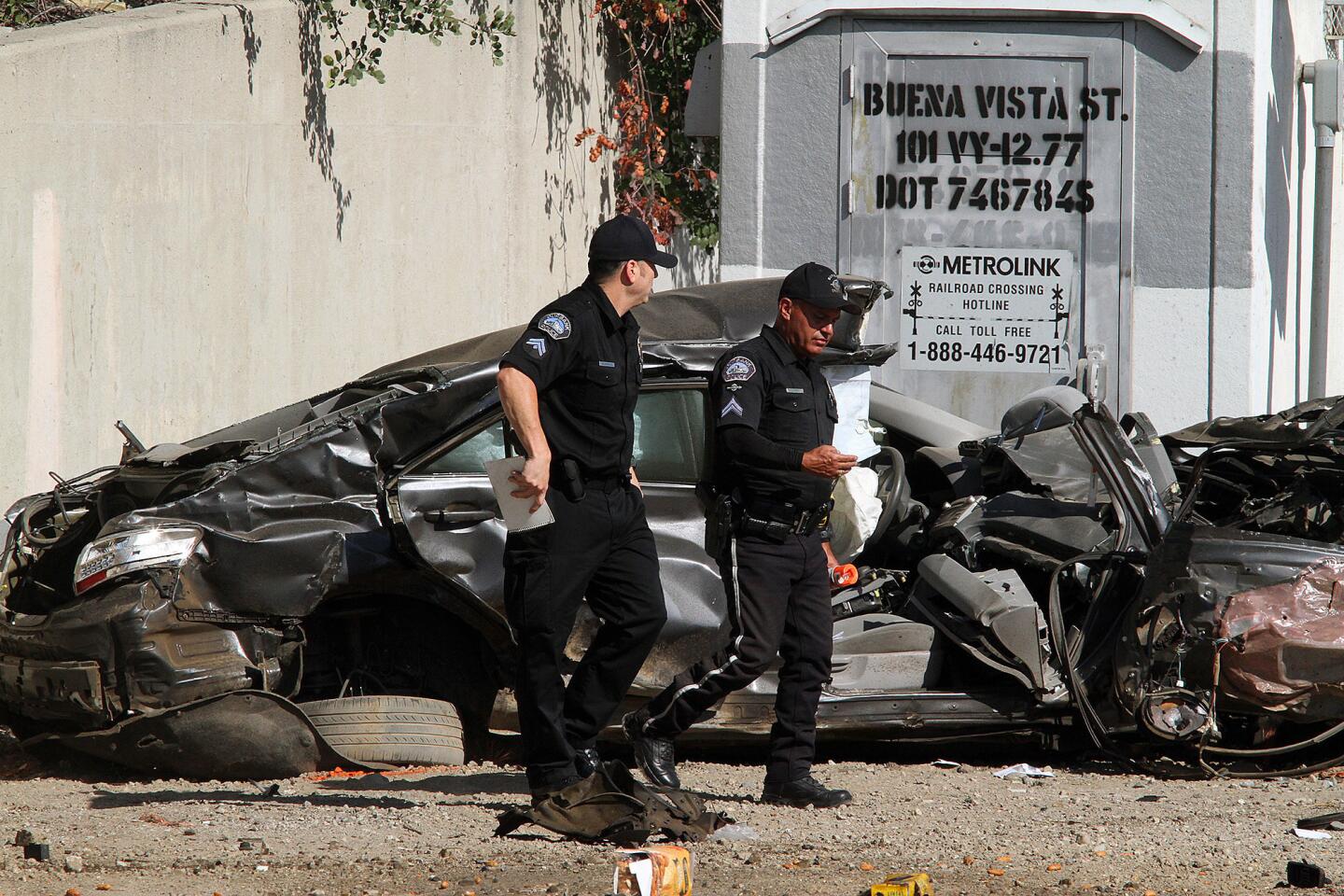 Two Burbank police officers walk passed a mangled vehicle resting off from the intersection of San Fernando and Buena Vista in Burbank after being clipped by a MetroLink train on Monday, September 2, 2014.
