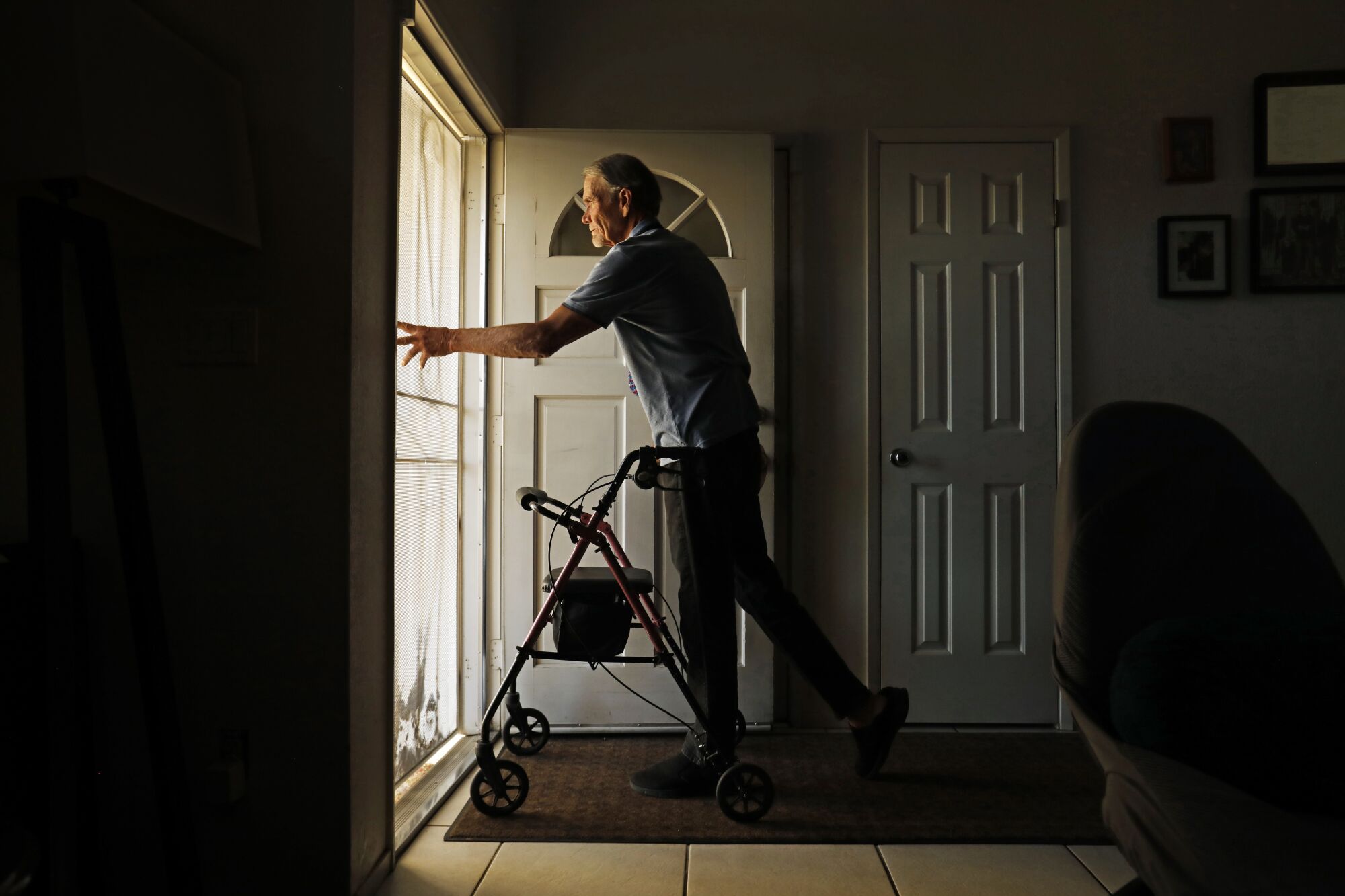 A man using a walker prepares to open a screen door as he leaves home.