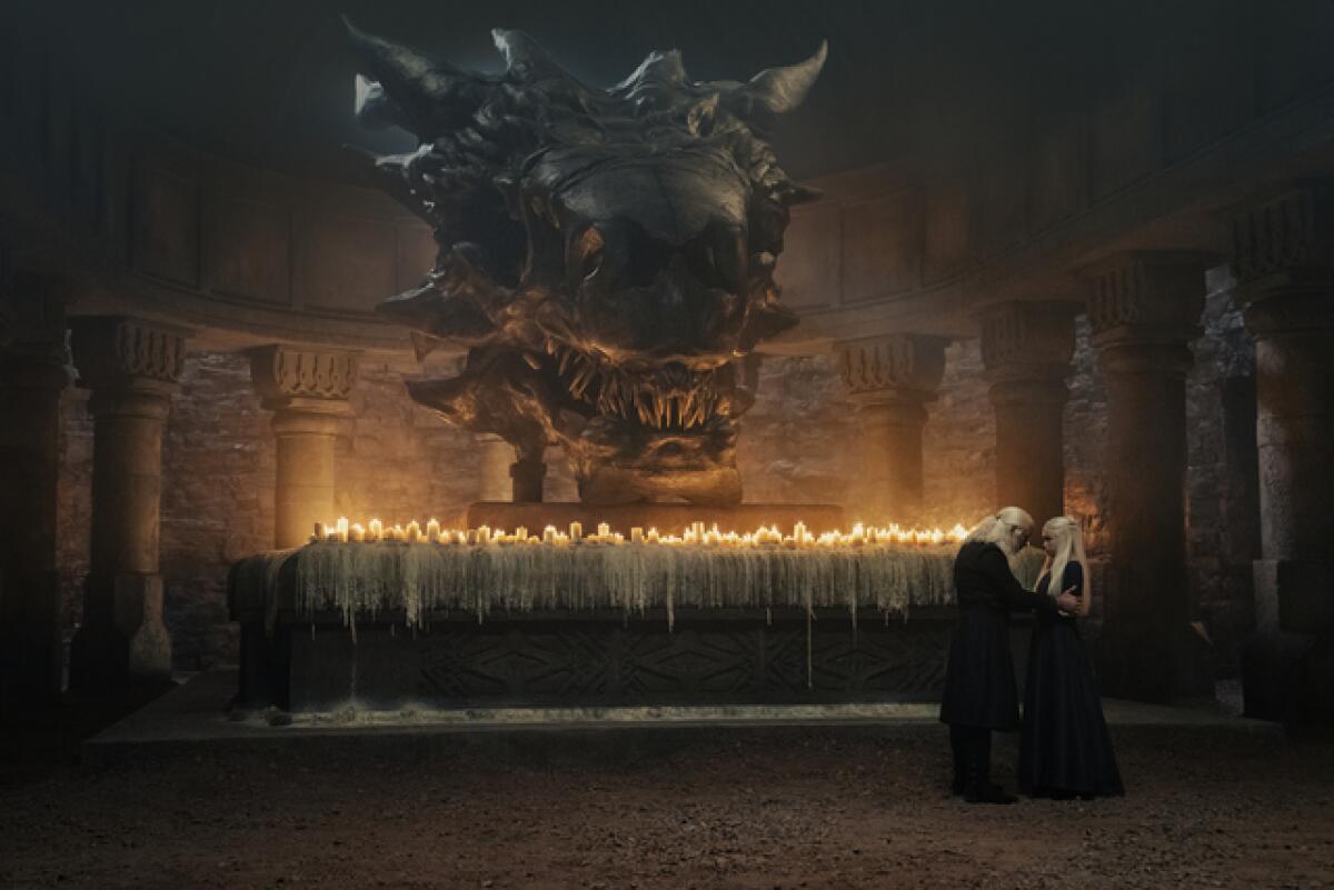 A father and daughter in deep discussion in a candlelit room with a stone dragon above them