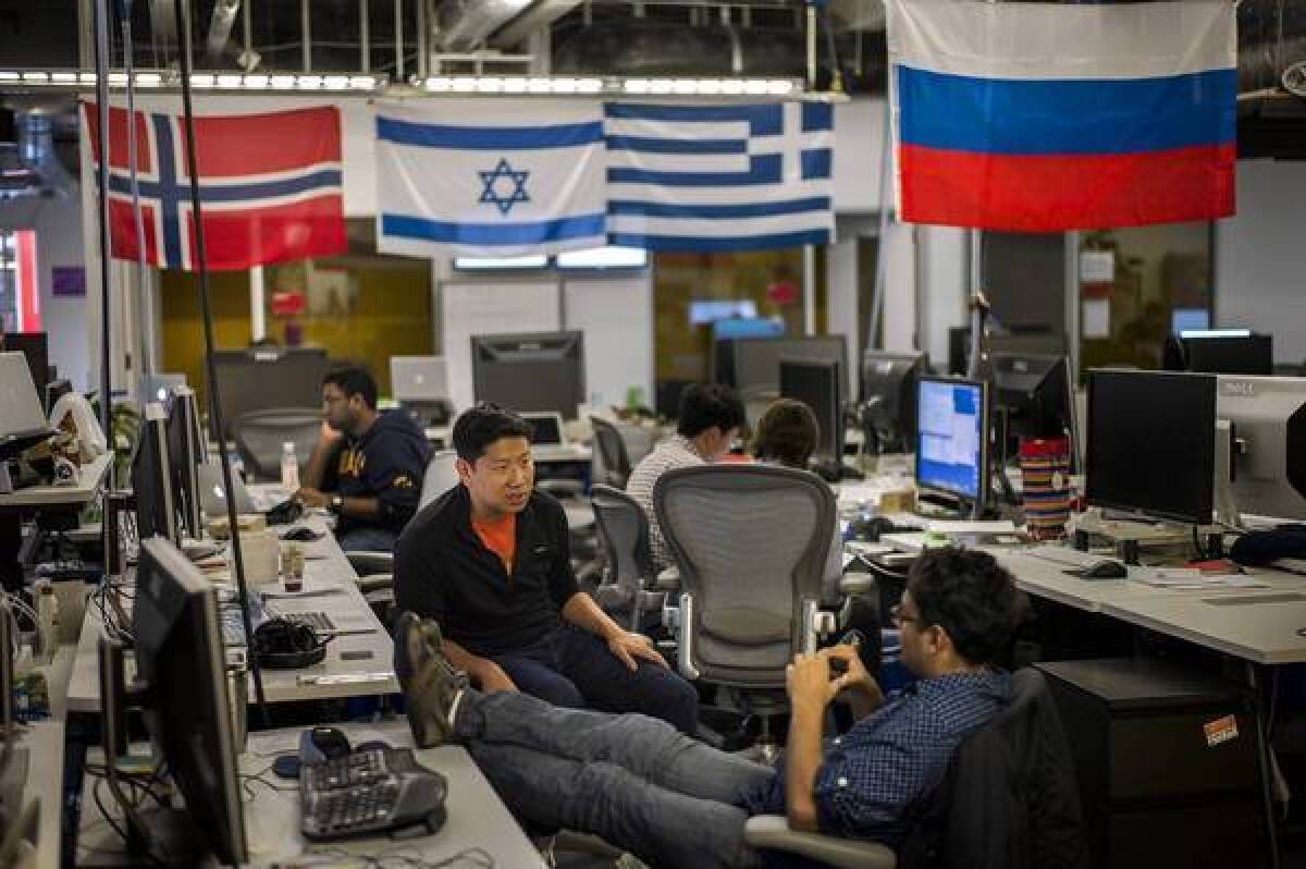 Sitting below flags from around the world, growth team member George Lee, left, speaks with Vishu Gupta at Facebook's Menlo Park headquarters. The company is pushing its global reach.