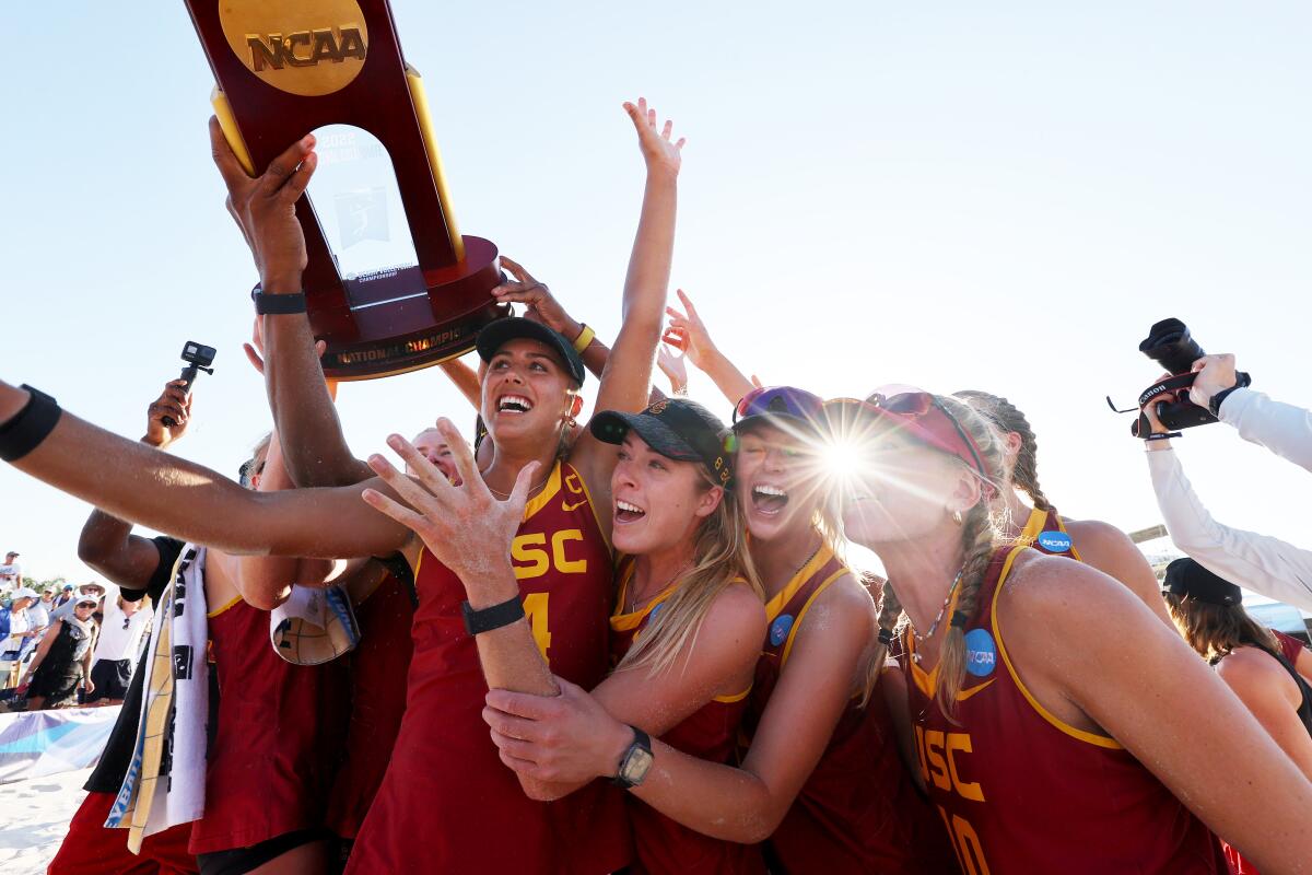 A group of women in red jerseys celebrate while holding a trophy with the word NCAA