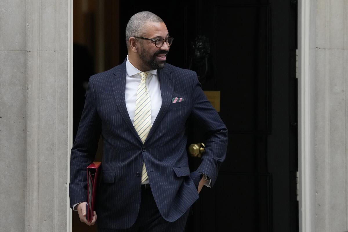 Britain's Home Secretary James Cleverly in a suit while standing in front of a door.