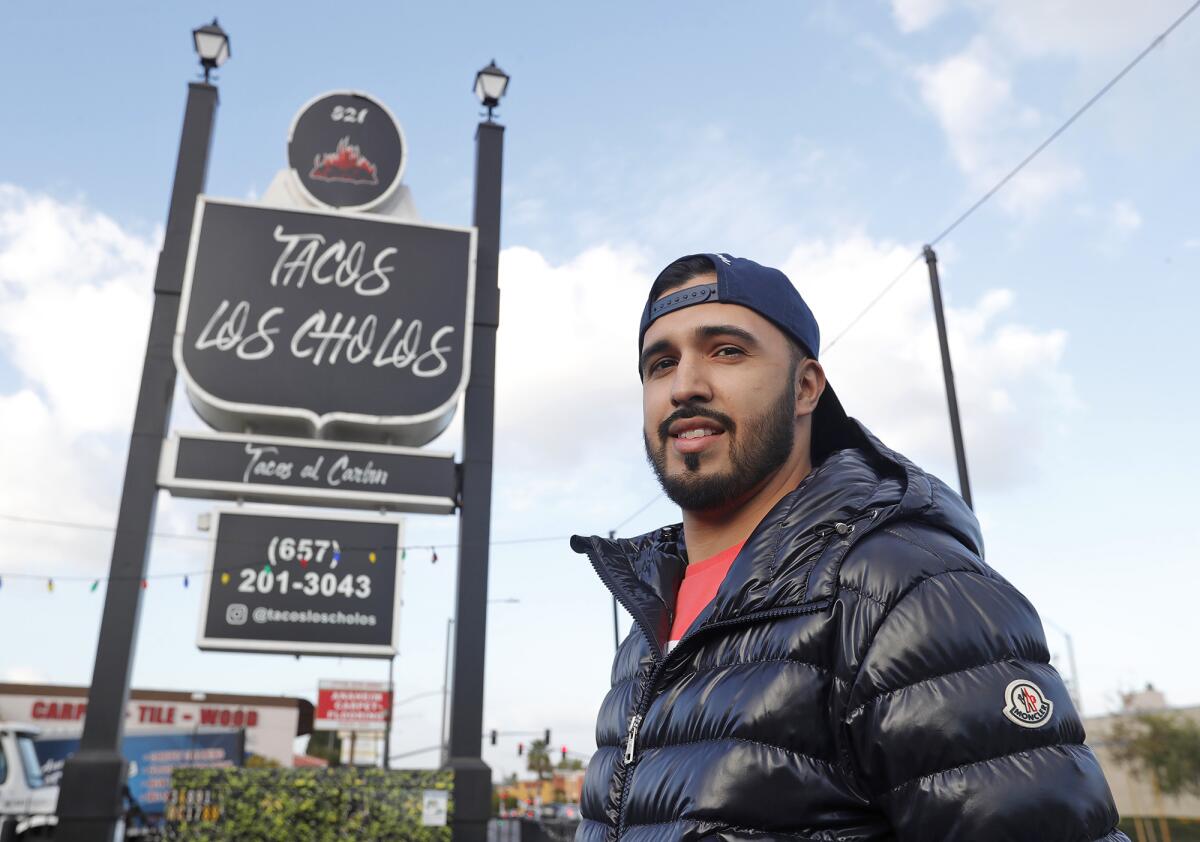 Co-owner Michael Alvarado stands under the sign at Tacos Los Cholos at the Anaheim location on Tuesday.