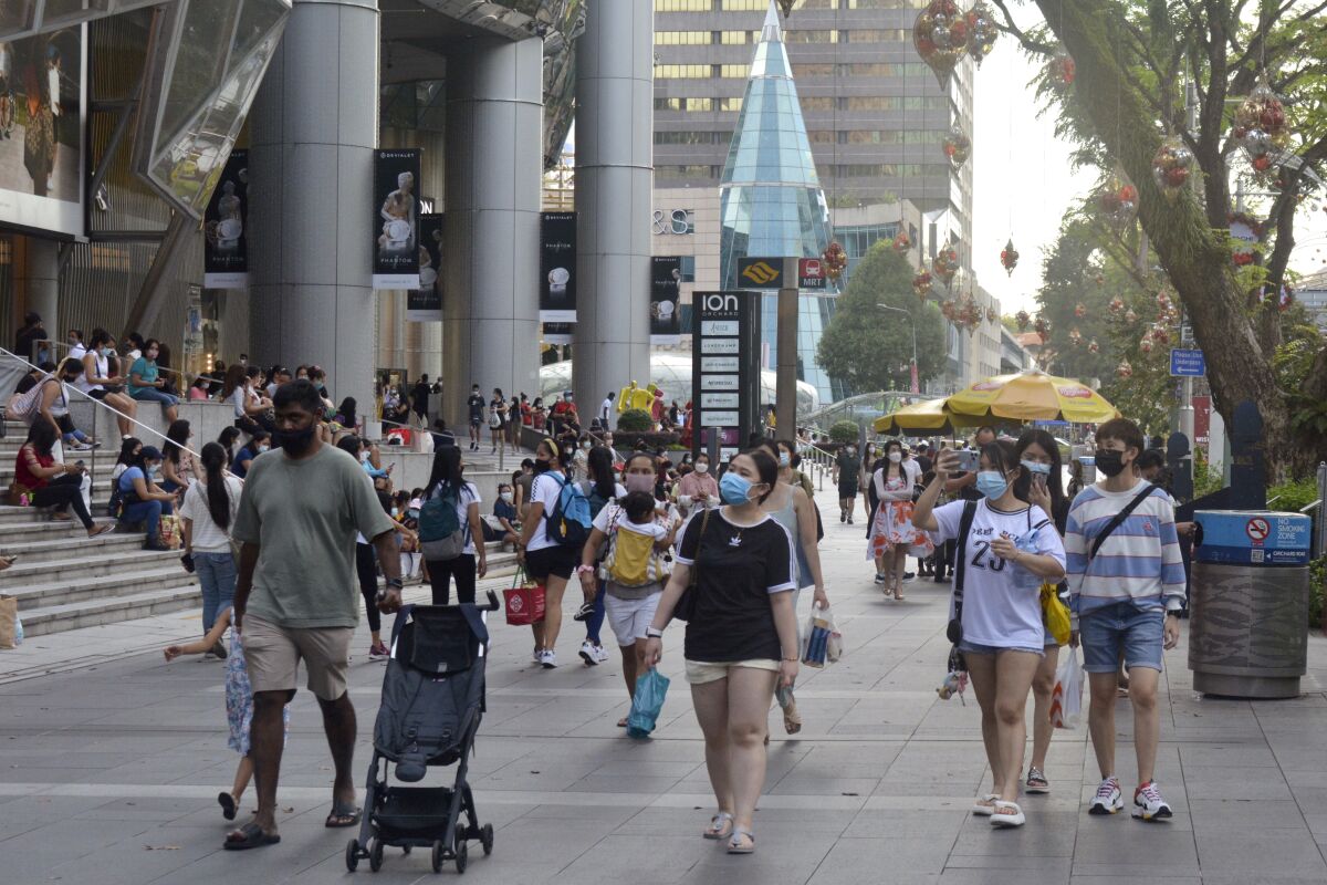 People wearing protective face masks walk along the Orchard Road shopping area in Singapore on Nov. 28, 2021. When Singapore embarked upon its strategy of “living with COVID,” backed by one of the world's leading vaccine programs, the wealthy city-state saw a spike in its rate of infections, leading many to question whether the time was right. (AP Photo/Annabelle Liang)
