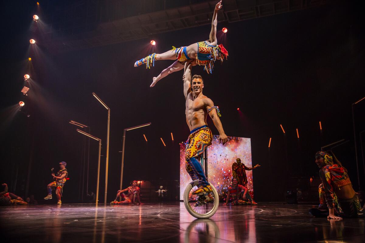 A man on a unicycle holds a performer above his head using one arm.