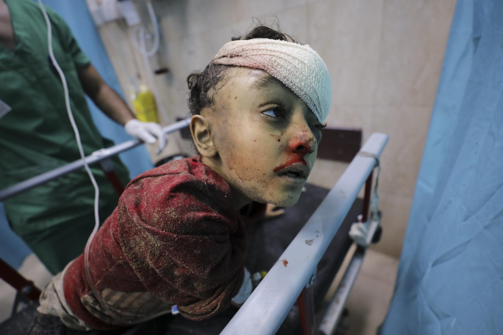 Palestinian child with bandaged head and bloodied face in Gaza hospital