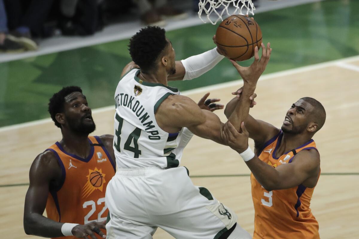 Milwaukee Bucks forward Giannis Antetokounmpo (34) drives to the basket between Phoenix Suns center Deandre Ayton (22) and guard Chris Paul (3) during the second half of Game 4 of basketball's NBA Finals Wednesday, July 14, 2021, in Milwaukee. (AP Photo/Aaron Gash)