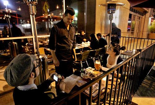Rolando Maldonado waits on customers Jeff Valenzuela and Kristine Arellano on the outside patio at Lazy Ox Canteen on the edge of Little Tokyo in downtown Los Angeles.