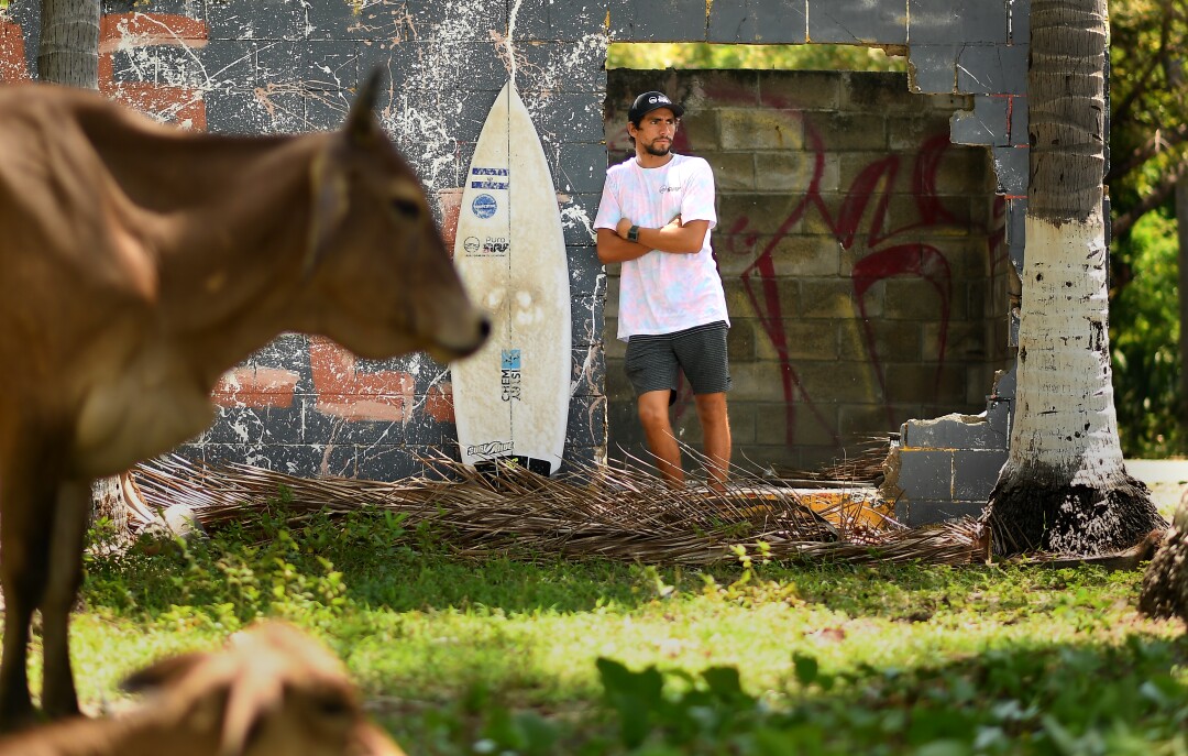 Surfer Perez stands with his board in the Rio Mar community of El Salvador
