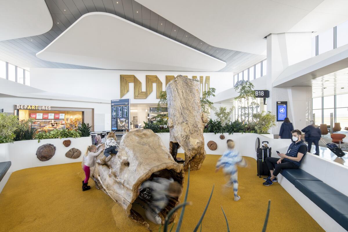 Children clamber around a pair of large logs in a soft-floored play area inside an airport terminal.