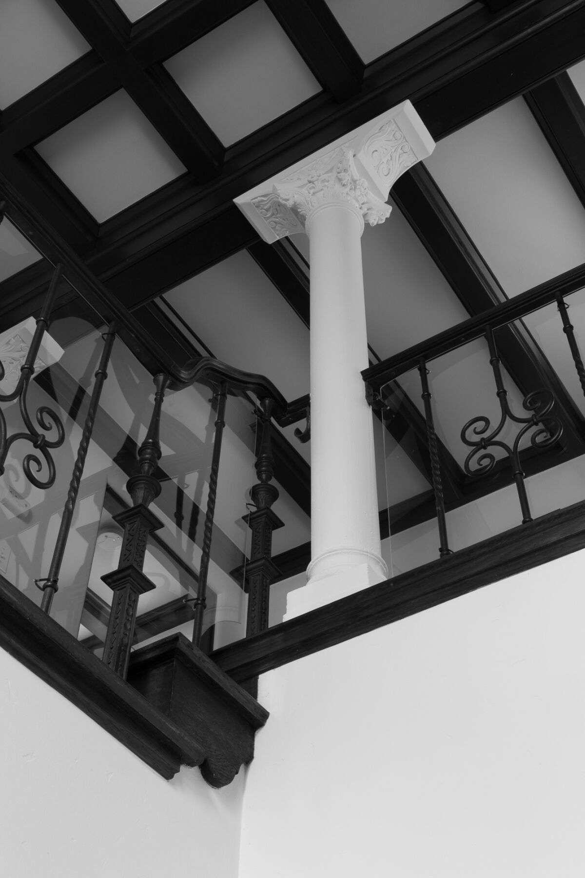 A black and white image shows a Corinthian column extending into a wood beam ceiling
